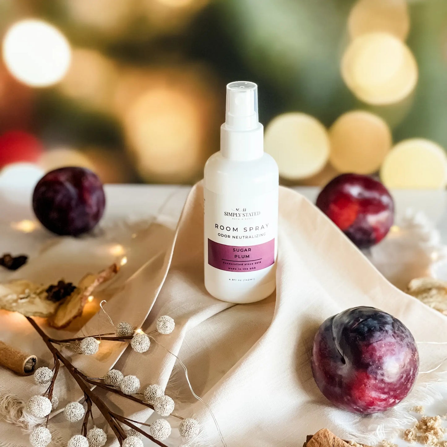 Room spray bottle on a decorative surface with plums and berries, blurred lights in the background