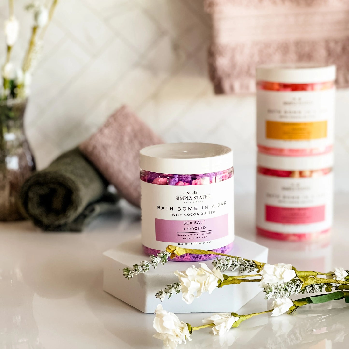 Bath bomb in a jar with decorative packaging on a marble surface with flowers.