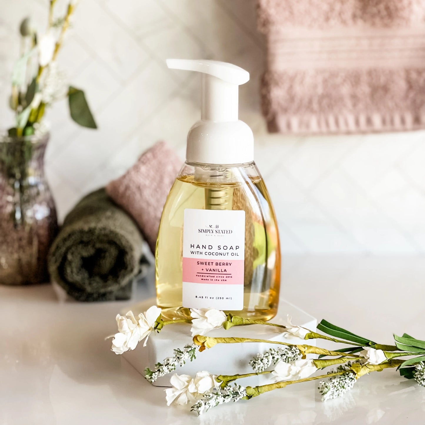 Hand soap bottle with a label on a surface with flowers and towels in the background