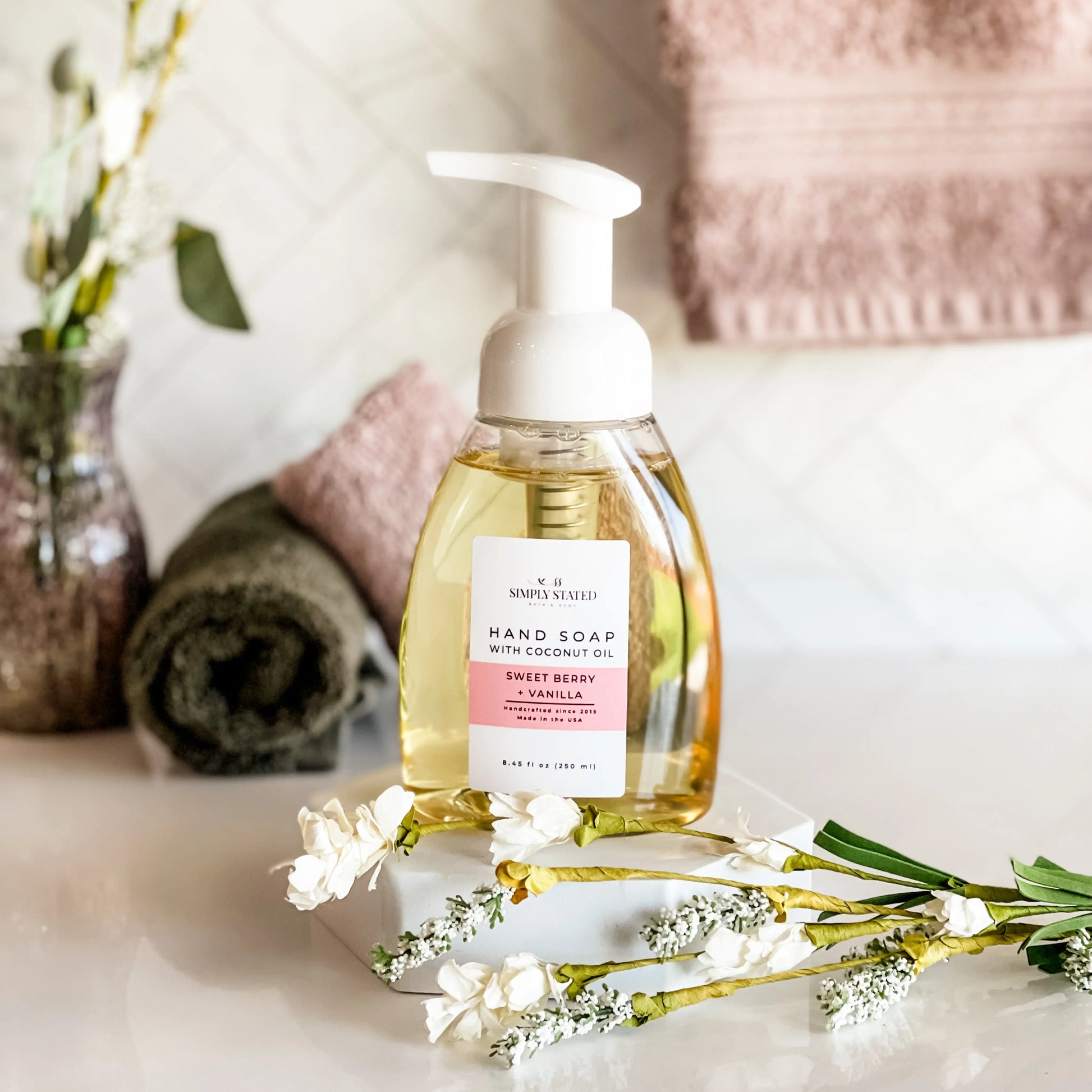 Hand soap bottle with a label on a surface with flowers and towels in the background