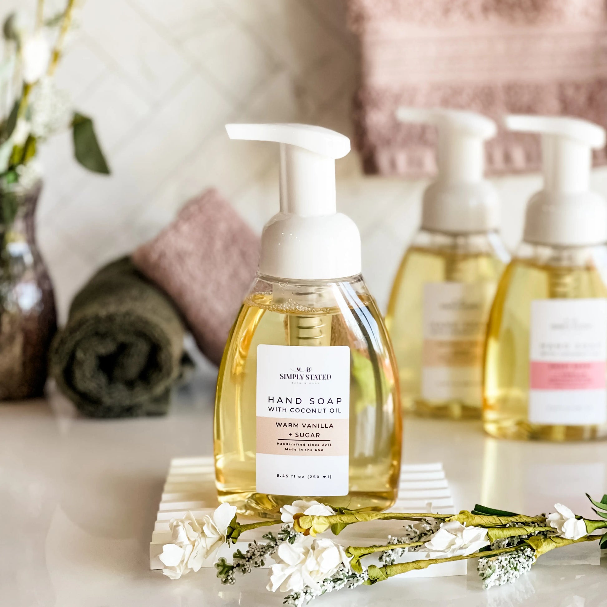 Hand soap bottle with pump dispenser on a decorative stand with flowers and soft background