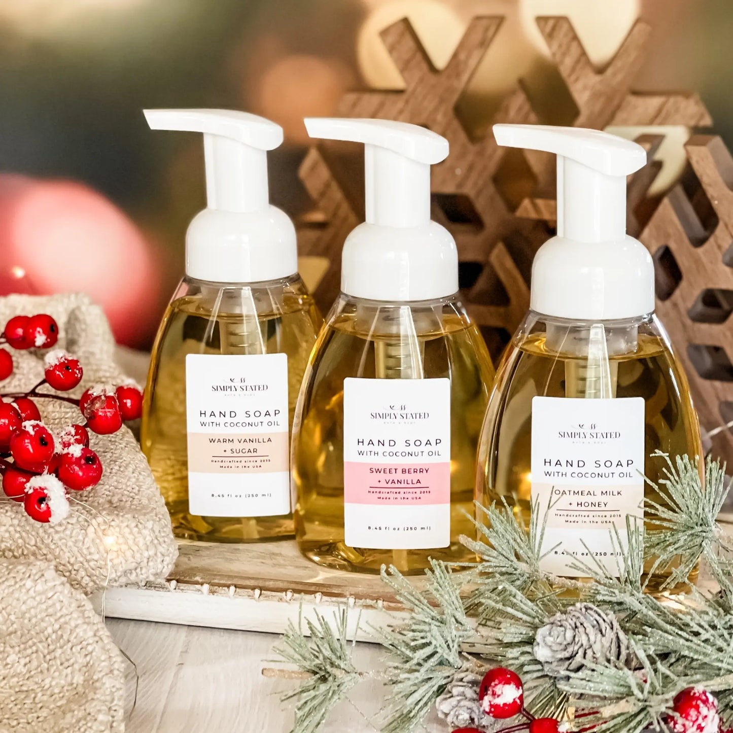 Three bottles of hand soap with pump dispensers on a decorative surface with Christmas elements.