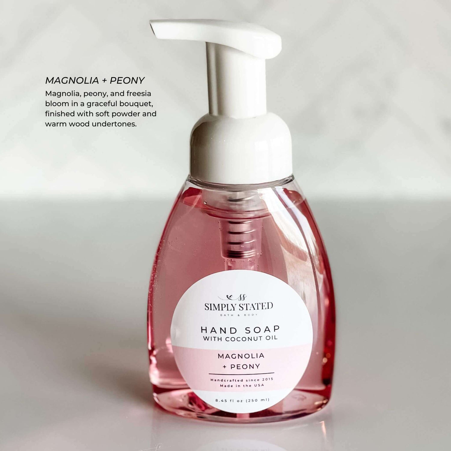 Pink-tinted bottle of Magnolia + Peony Hand Soap, featuring a floral fragrance with notes of peony, magnolia, and freesia.