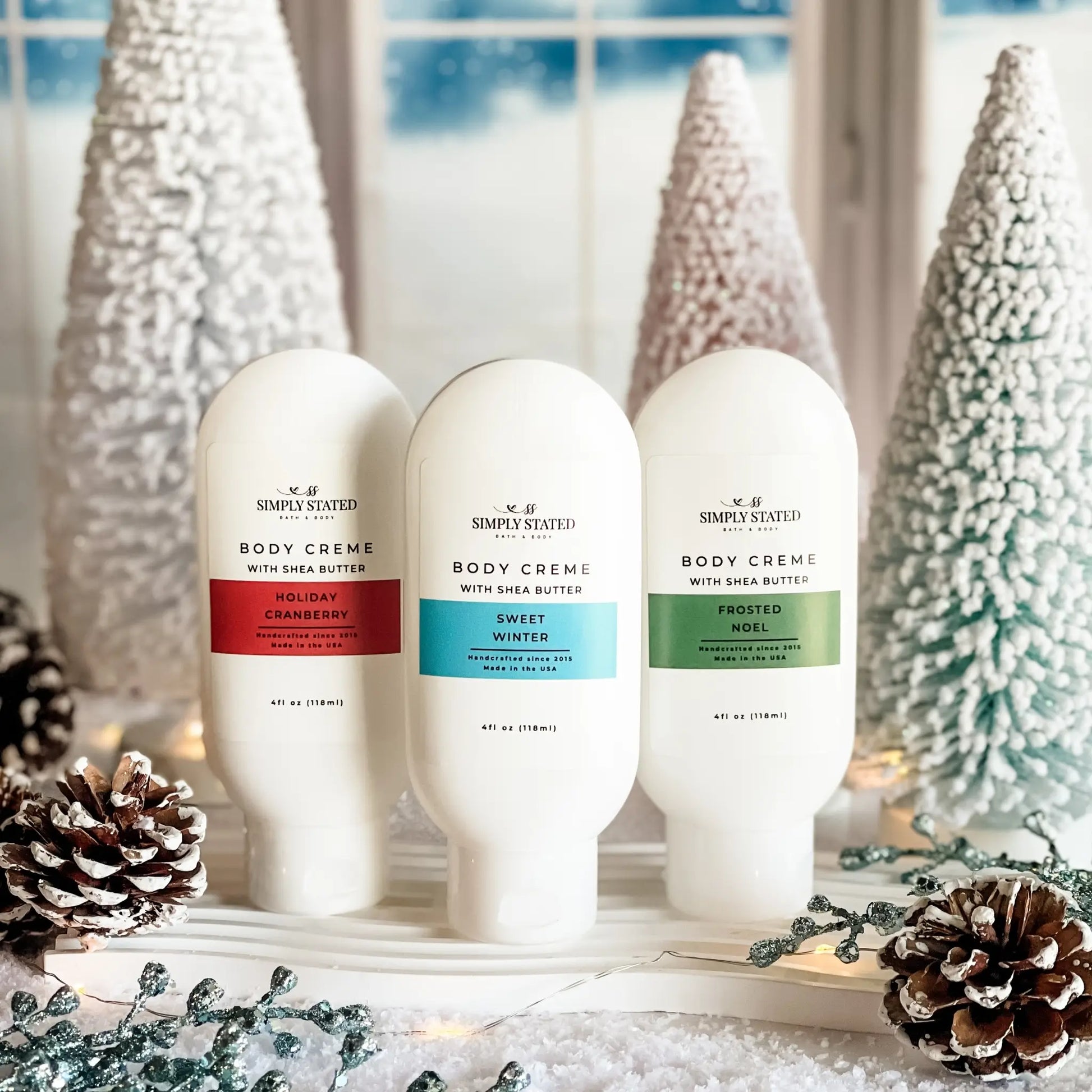 Three bottles of Simply Stated Body Creme with Christmas decorations in the background