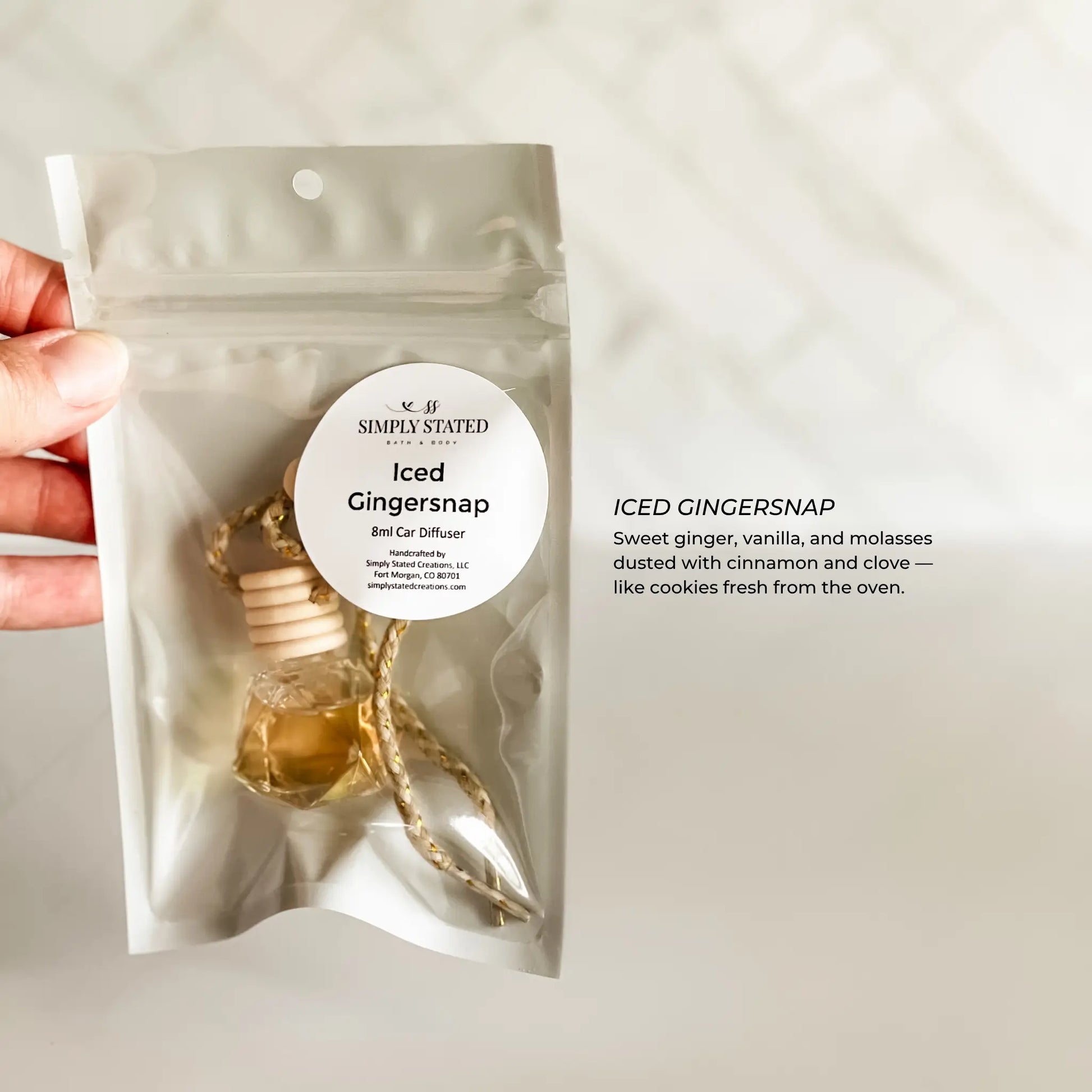Hand holding a 'Simply Stated' iced gingersnap car diffuser package against a neutral background.
