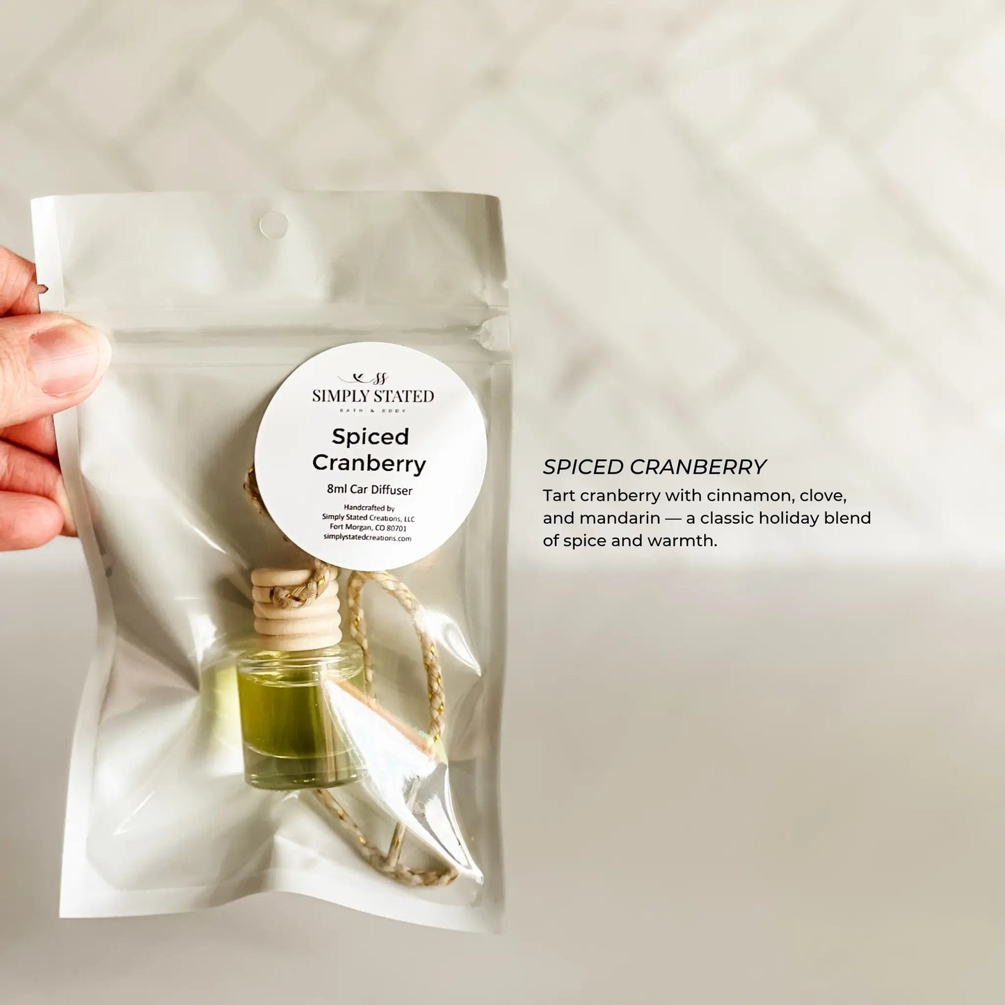 Spiced Cranberry car diffuser package held by a hand on a neutral background