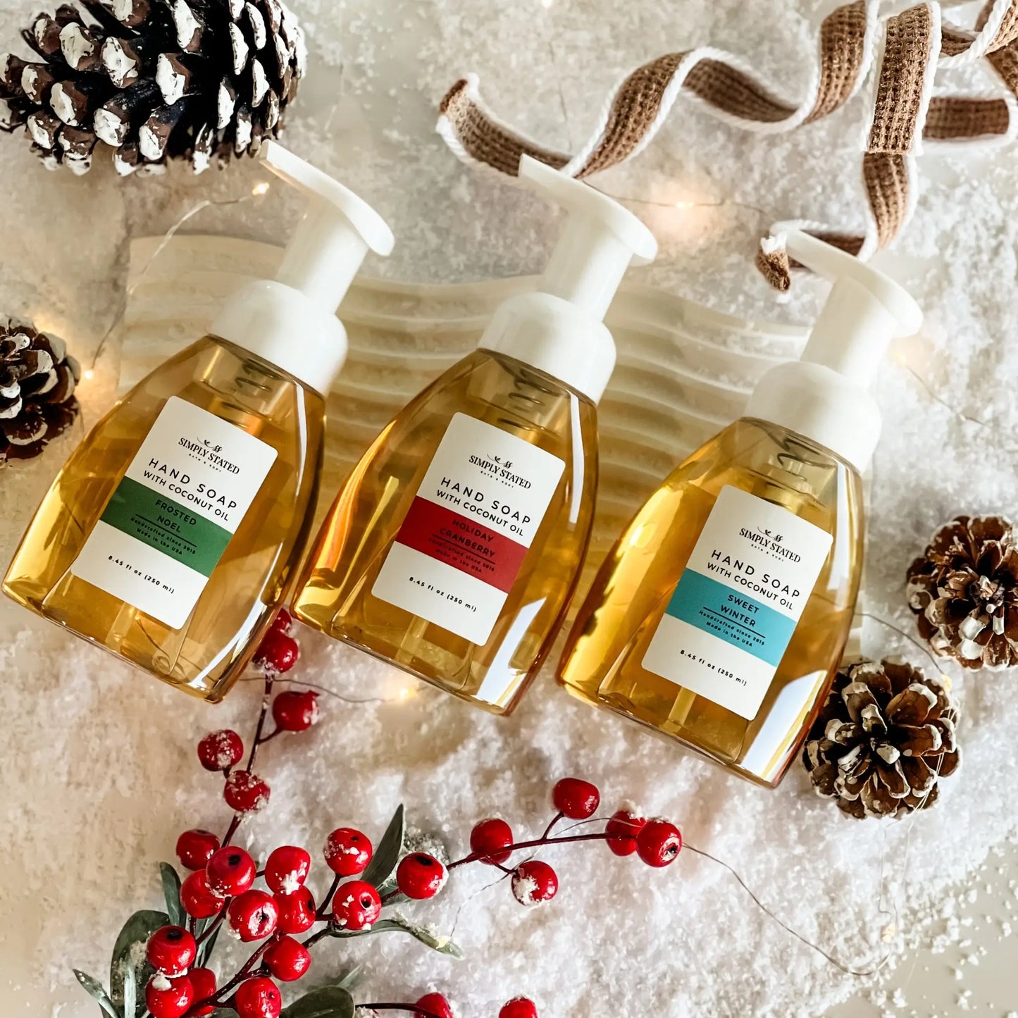 Three bottles of hand soap with pump dispensers on a decorative background with pine cones and berries.
