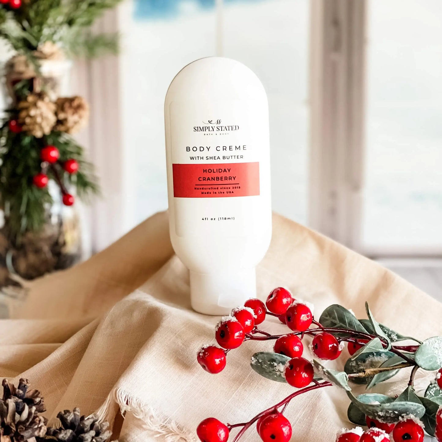 Body cream bottle with holiday cranberry design on a beige surface with decorative elements.