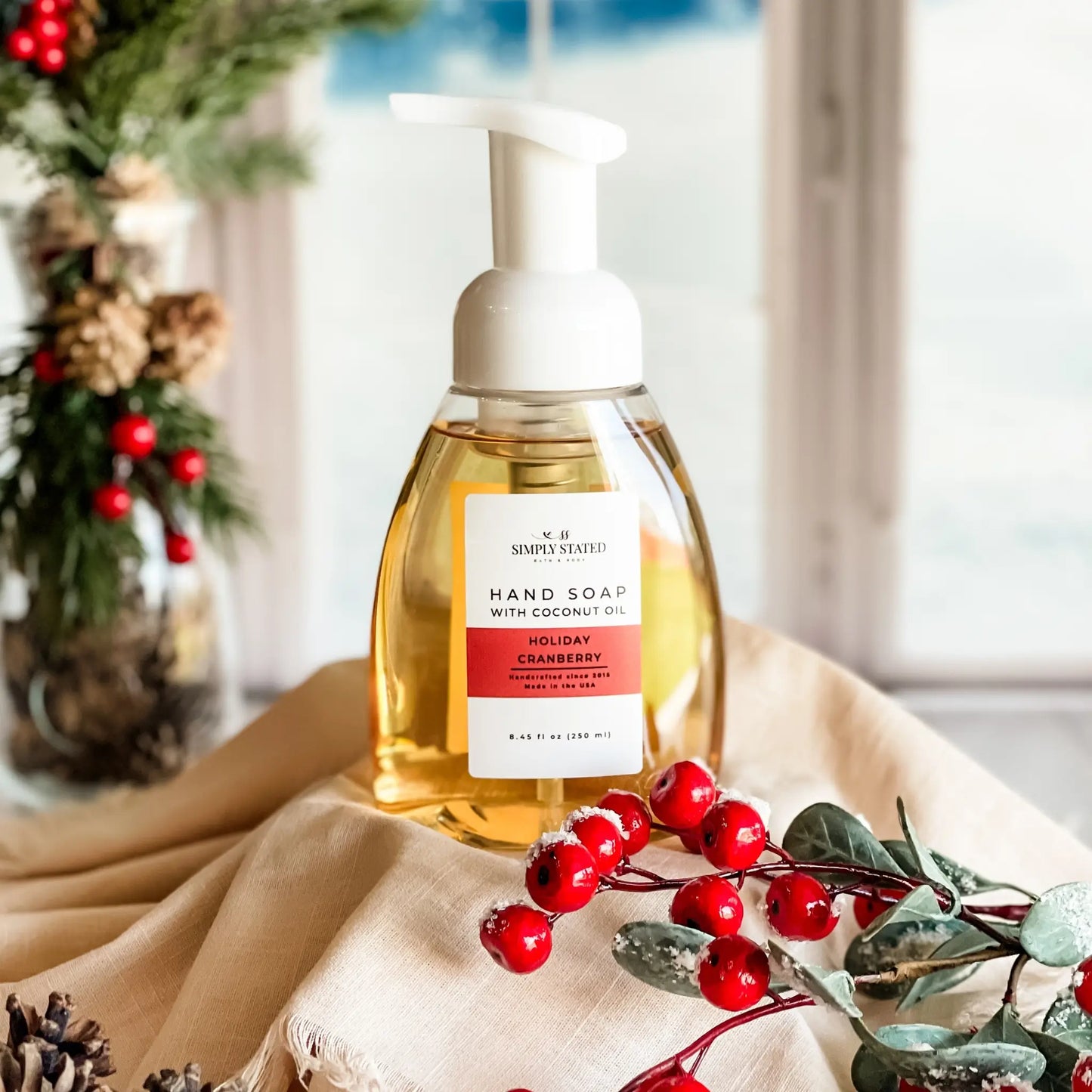 Hand soap bottle with holiday design on a table with red berries and greenery.
