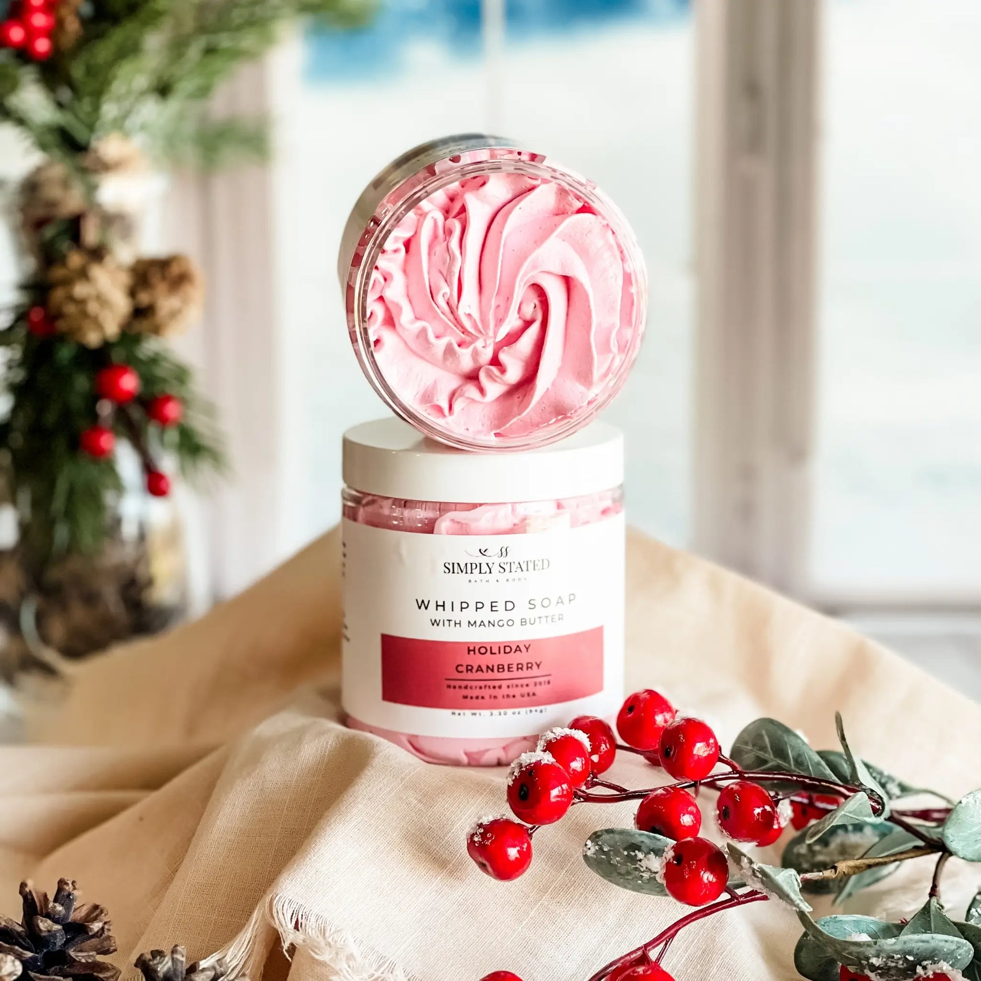 Whipped soap container with pink swirl design on a decorative surface with Christmas elements.