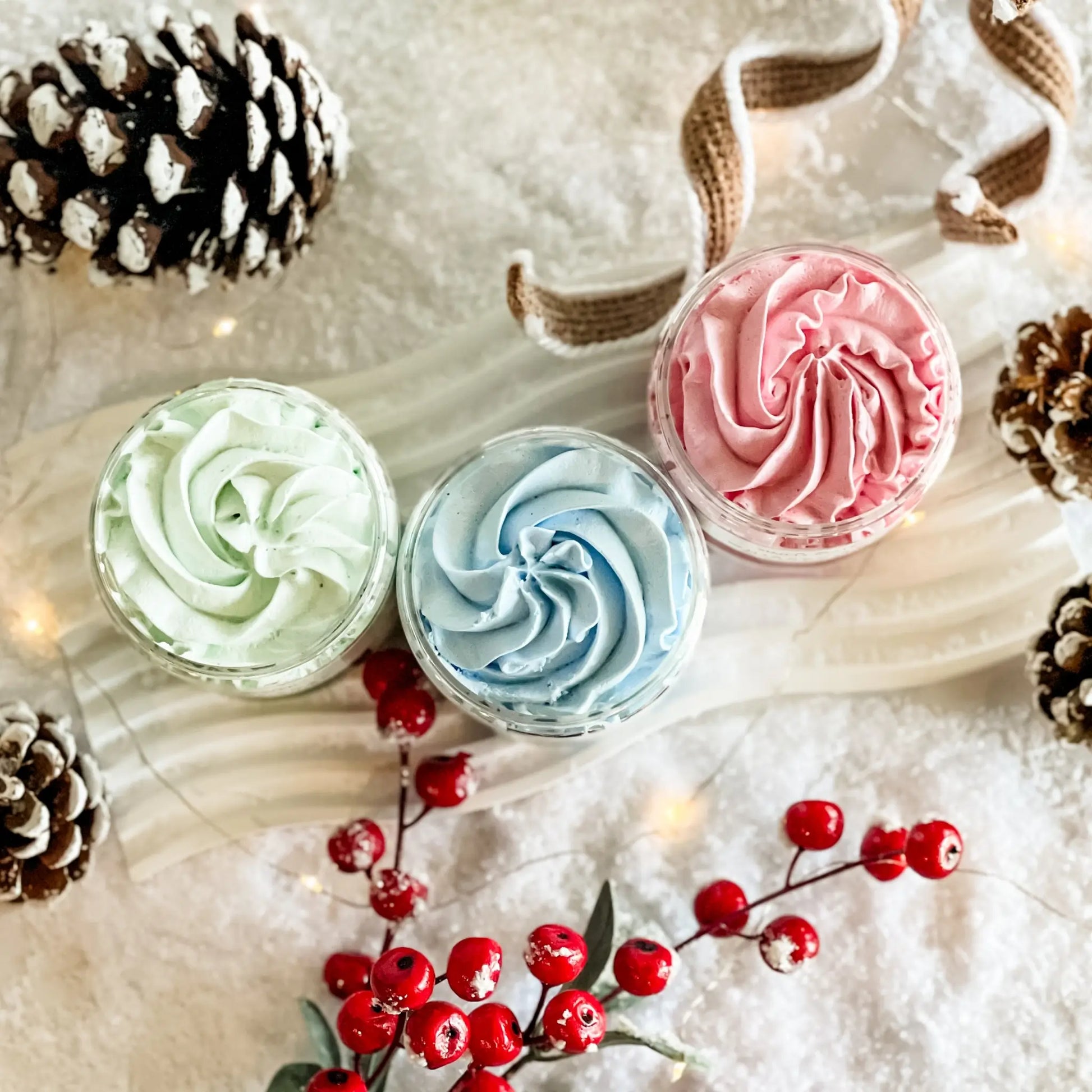Three small containers with swirled frosting on a snowy background with pinecones and berries.