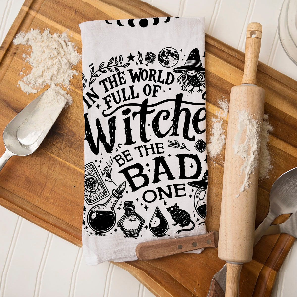 in a world full of witches be the bad one towel on cutting board
snarky witch kitchen décor towel for spooky season
witchcore kitchen towel with broom moon and potion illustrations